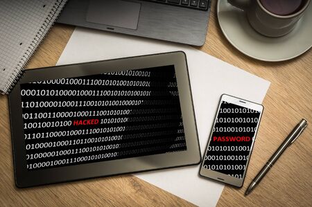 Digital tablet on business table with hacked binary code on screen and mobile phone, paper, pen, laptop and cup of coffee - above viewの写真素材