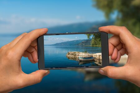 Woman hands with mobile cell phone to take a photo of Ohrid lake in Macedoniaの写真素材