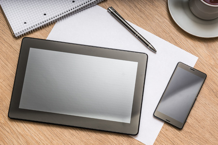 Workplace with digital tablet, mobile phone, paper, pen, note and cup of coffee on wooden table - above viewの写真素材