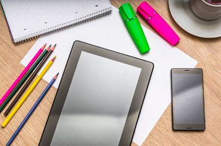 Workplace with digital tablet, mobile phone, paper, pencils and cup of coffee on wooden table - above viewの写真素材