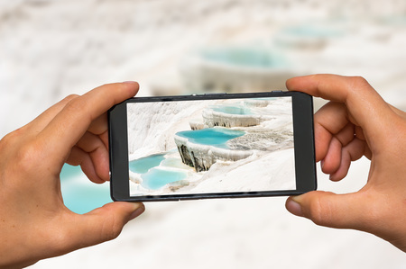 Woman hands with mobile cell phone to take a photo of mineral springs in Turkey, Pamukkaleの写真素材