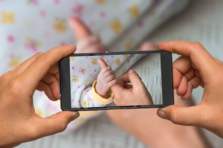 Woman hands with mobile cell phone to take a photo of newborns fingers touching mothers handの写真素材