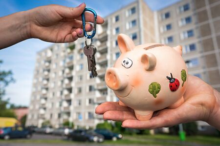Real estate agent giving flat keys to a new property owner, who is paying last saving money from piggy bank on blurred backgroundの写真素材