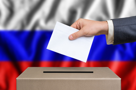 Election in Russia. The hand of man putting his vote in the ballot box. Russian flag on background.の写真素材