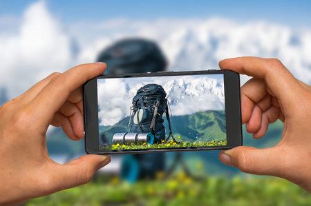 Woman hands with mobile cell phone to take a photo of tourist backpack, sleeping pad and mountains in Georgiaの写真素材