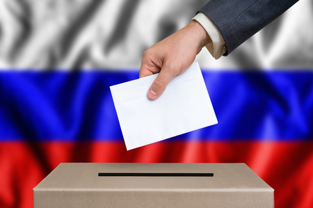 Election in Russia. The hand of man putting his vote in the ballot box. Russian flag on background.の写真素材