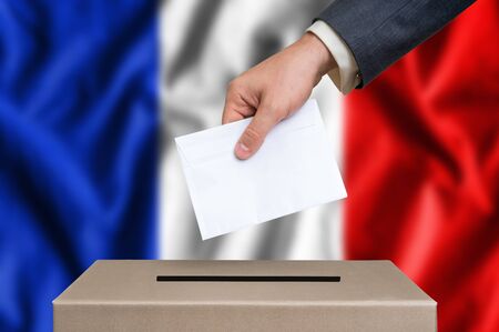 Election in France. The hand of man putting his vote in the ballot box. French flag on background.の写真素材