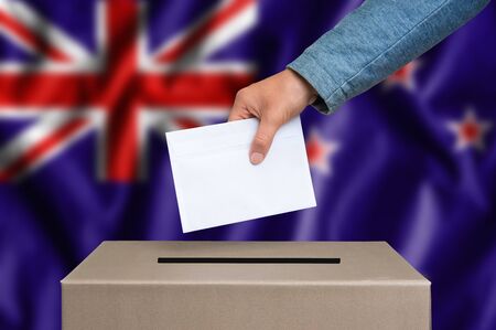 Election in New Zeland. The hand of woman putting her vote in the ballot box. New Zeland flag on background.の写真素材