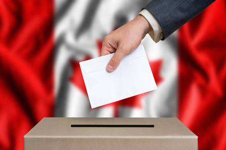 Election in Canada. The hand of man putting his vote in the ballot box. Canadian flag on background.の写真素材