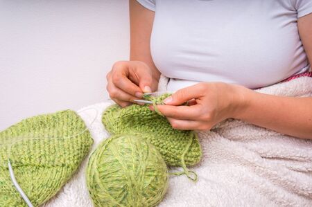 Woman hands with needles knitting with green wool at homeの写真素材