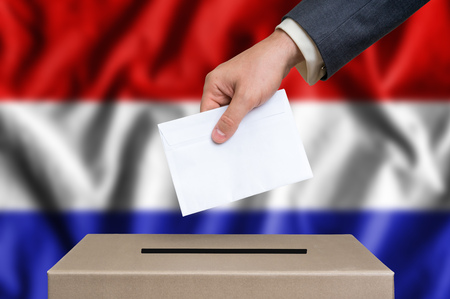 Election in Netherlands. The hand of man putting his vote in the ballot box. Dutch flag on background.の写真素材