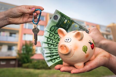 Real estate agent giving house keys to a new property owner, who is paying by euro money on blurred backgroundの写真素材