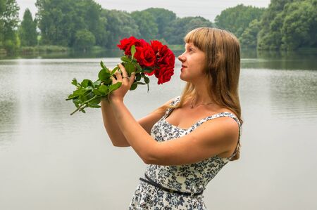 Beautiful young lady by the lake holds a rosesの写真素材