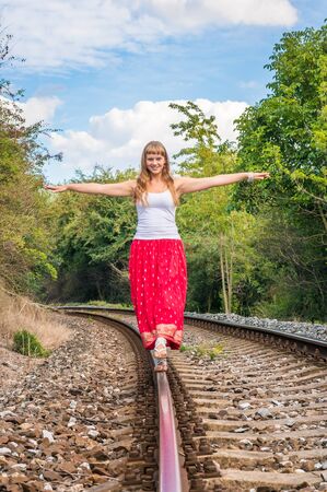 Young lady in red dress walking on railway tracksの写真素材