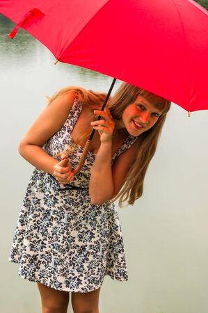 Beautiful young lady with red umbrella near the pondの写真素材