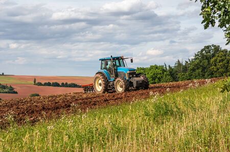 Farmer in blue tractor working on a fieldの写真素材