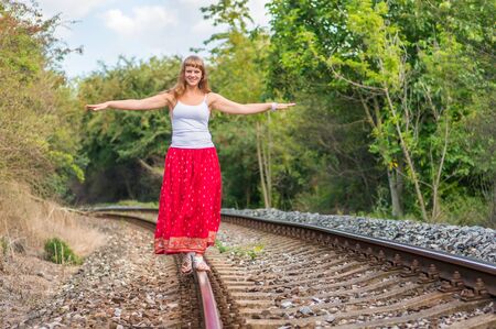 Young lady in red dress walking on railway tracksの写真素材