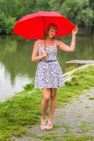 Beautiful young lady with red umbrella near the pondの写真素材