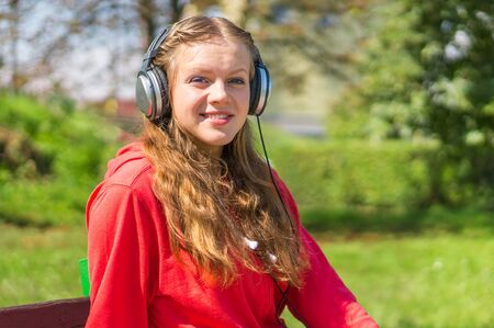 Young lady listening to music and relaxing on a park benchの写真素材