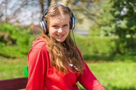 Young lady listening to music and relaxing on a park benchの写真素材