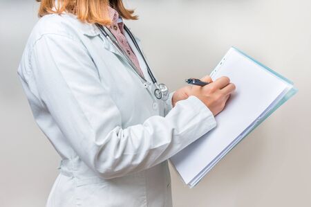 Female doctor with stethoscope writing to clipboardの写真素材