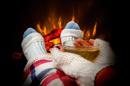Woman resting with cup of tea near fireplace at homeの写真素材