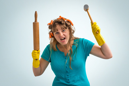 Crazy housewife with kitchen roller and meat hammer isolated on blue backgroundの写真素材
