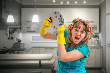 Aggressive housewife woman with yellow rubber gloves washing dishes in kitchenの写真素材