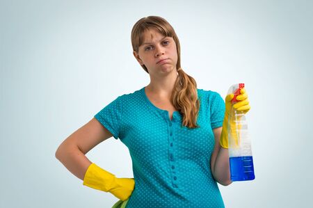Tired housewife woman in yellow gloves with a rag and detergent on blue backgroundの写真素材
