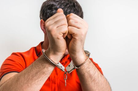Arrested man in handcuffs hidden his face in front of cameraの写真素材