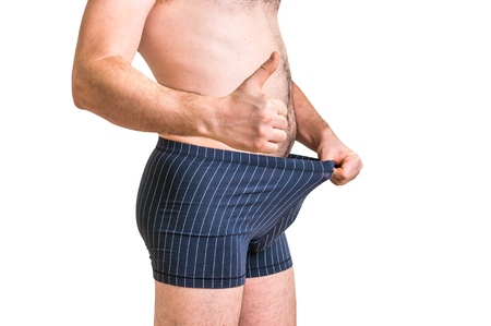 Attractive man is looking in his boxer underwear and pointing thumb up - isolated on white backgroundの写真素材