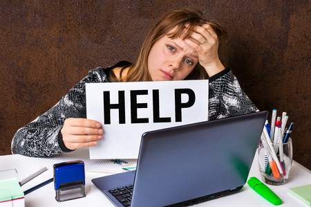 Overworked woman in stress working on her laptop and asking for helpの写真素材