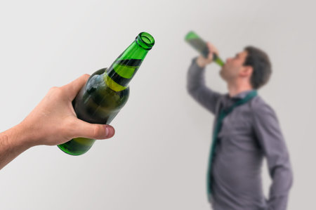Unfocused man drinking alcohol and another man holding a bottle of beer on gray background