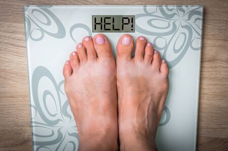 Woman's feet on a scale with word HELP! - obesity conceptの写真素材