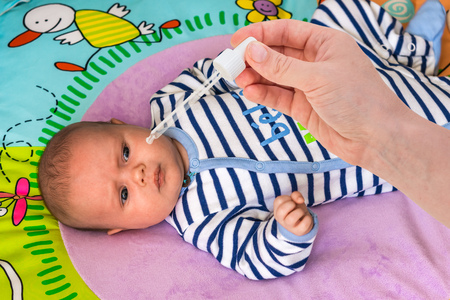 Newborn gets nose drops with saline solution in morningの写真素材
