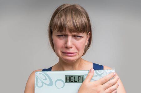 Frustrated overweight woman holding digital scales with word HELP! - diet and obesity conceptの写真素材