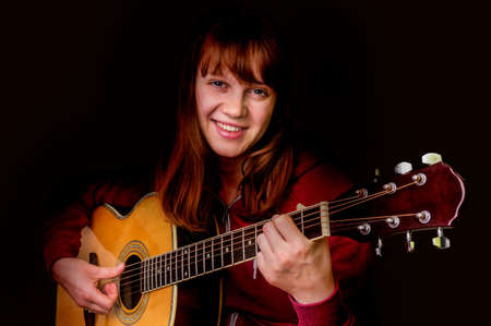 Young girl playing acoustic guitar - isolated on black backgroundの写真素材