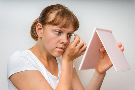 Young woman plucking eyebrows with tweezers in front of mirrorの写真素材