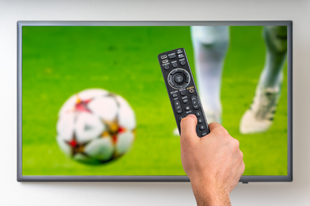 Man is watching football match on TV and holding tv remote controller in handの写真素材
