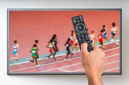 Man is watching running sports game on TV and holding tv remote controller in handの写真素材