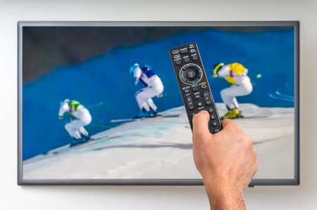 Man is watching winter skiing on TV and holding tv remote controller in hand