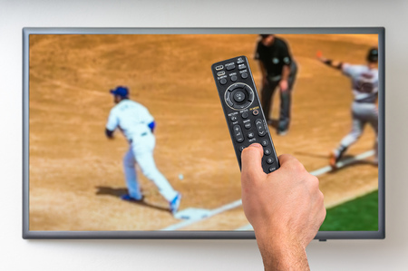 Man is watching baseball match on TV and holding tv remote controller in handの写真素材