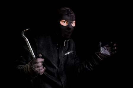 Masked thief in balaclava with crowbar isolated on black backgroundの写真素材