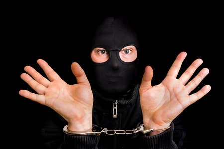 Masked thief in handcuffs isolated on black backgroundの写真素材
