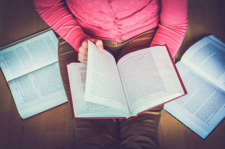 Young woman on the wooden floor in the library reading a book, studying - retro and vintage styleの写真素材