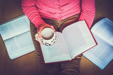 Woman hands holding a cup of coffee, she sits on the floor and studying from an open book - retro and vintage styleの写真素材
