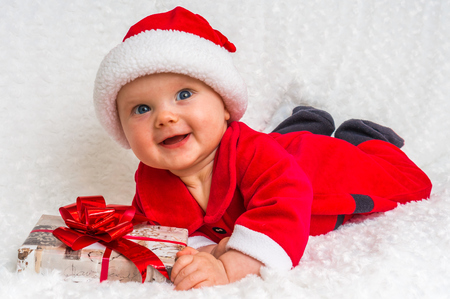 Funny Santa baby girl lying on white blanket with gift -  Christmas conceptの写真素材