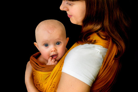 Happy mother with her baby in a sling - isolated on black background