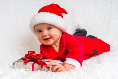 Funny Santa baby girl lying on white blanket with gift -  Christmas conceptの写真素材