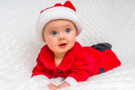Funny Christmas baby in Santa Claus costume lying on white blanketの写真素材